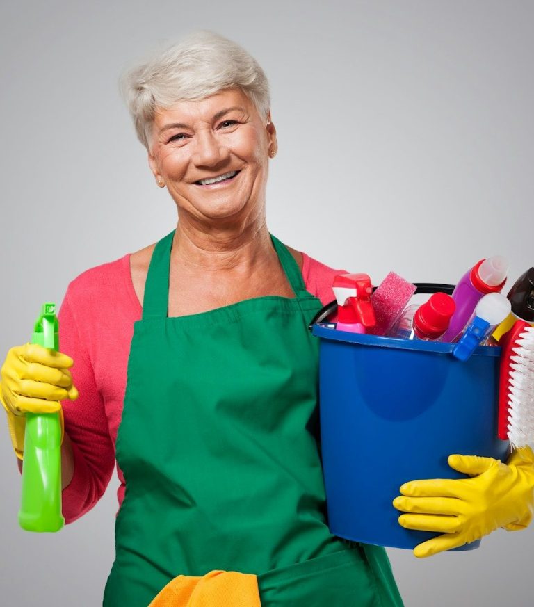 Ältere Frau mit Putzutensilien in der Hand und einem Eimer voller Reinigungsmittel.
