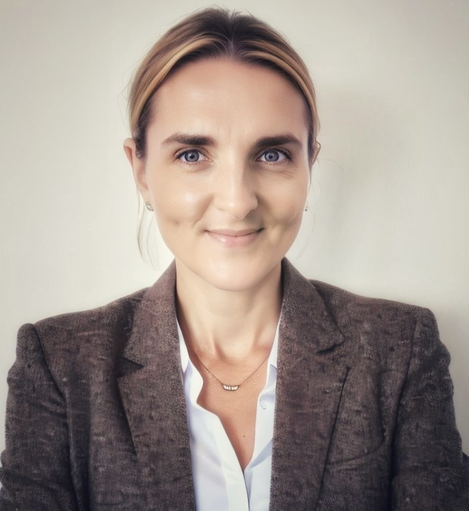 Frau mit blonden Haaren, leicht lächelnd, in einem hellen, neutralen Hintergrund.